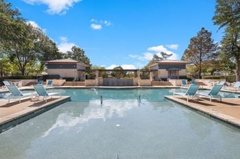 A large swimming pool with chairs and trees in the background